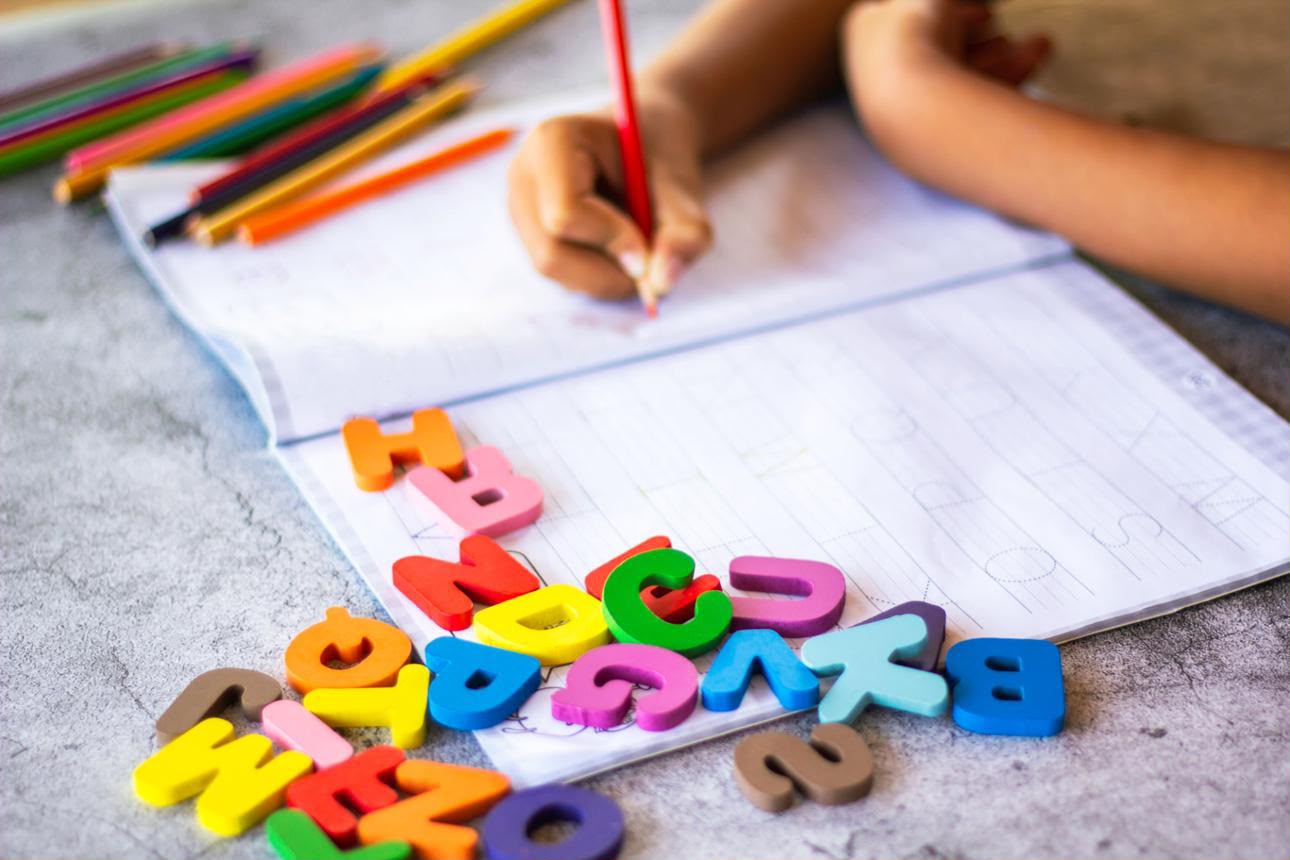 Criança escrevendo em caderno com letras coloridas